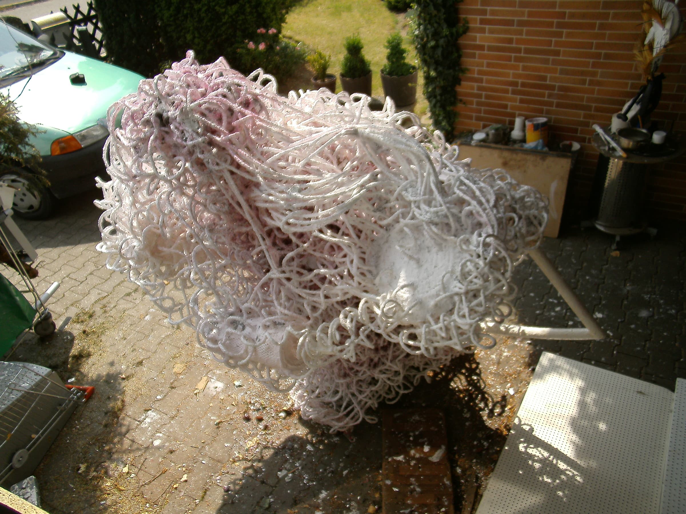 Rosa-weisse Schlingen-Skulptur mit weissem Rohrbogen in einem gepflasterten Hof vor einer Backsteinmauer