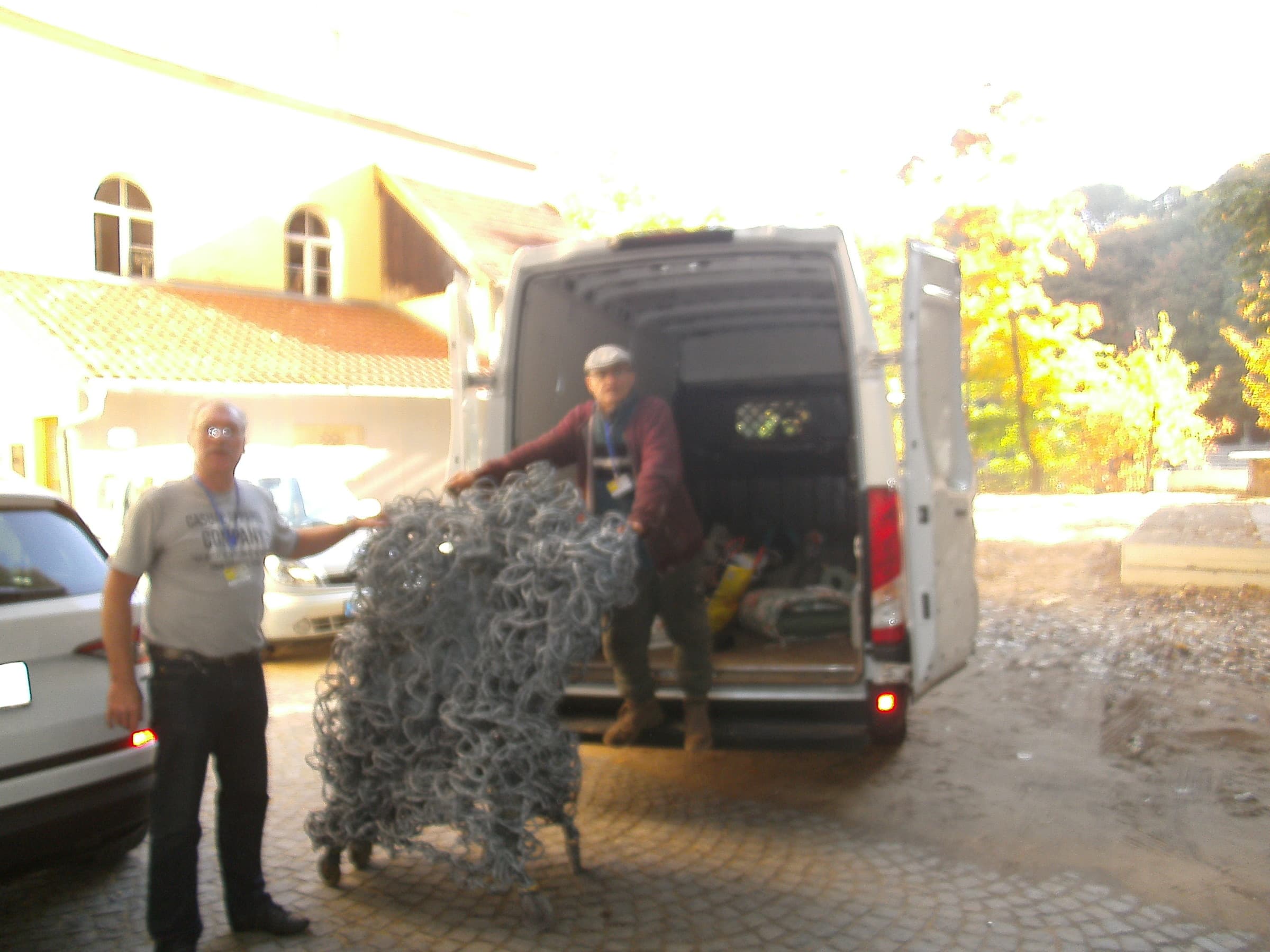 Zwei Männer laden eine graue Schlingen-Skulptur auf Rollen aus einem Transporter